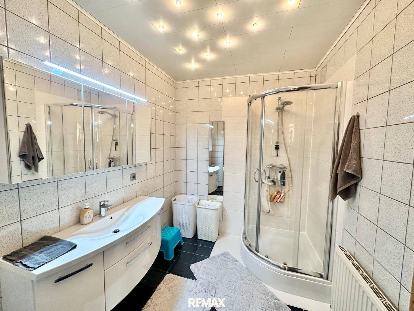 Modernes Badezimmer mit Duschkabine, Einzelwaschbecken und weißen Fliesen.
