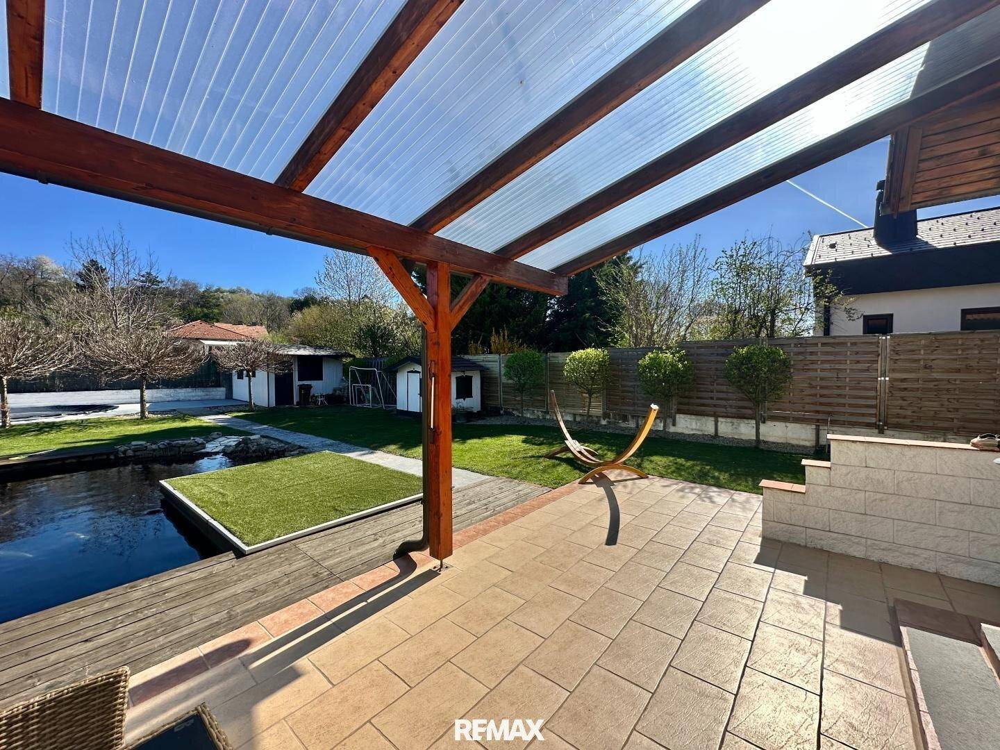 Geräumige, überdachte Terrasse mit Fliesenboden und Blick auf den Gartenbereich.