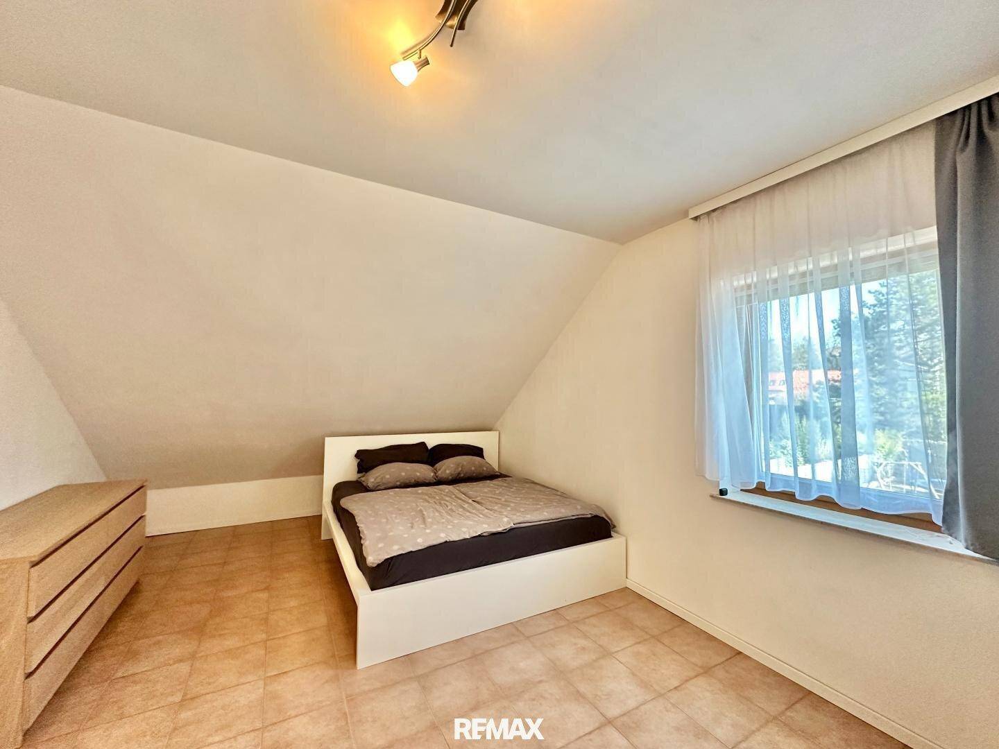 Helles Schlafzimmer im Dachgeschoss mit Bett, Kommode und Fliesenboden.