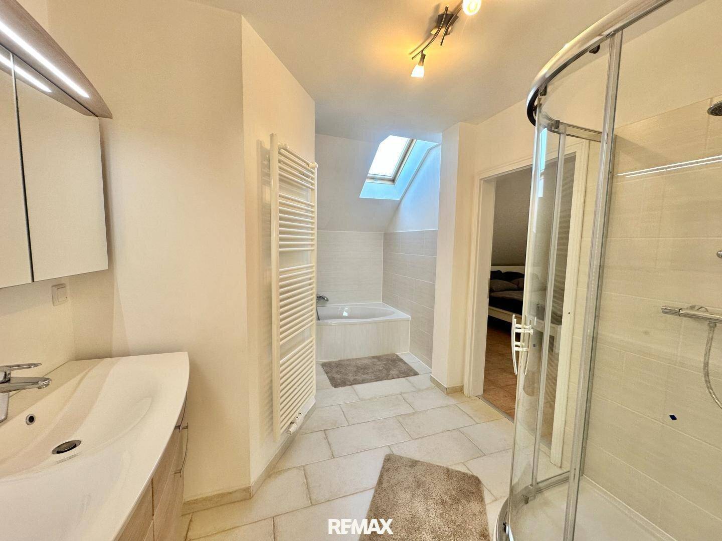 Modernes Badezimmer im Dachgeschoss mit Dusche, Badewanne und Dachfenster.