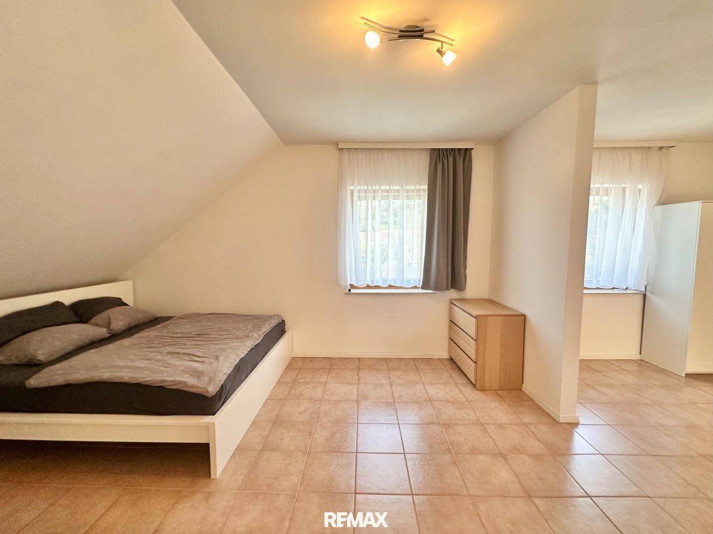 Geräumiges Schlafzimmer im Dachgeschoss mit Bett, Kommode und Fliesenboden.