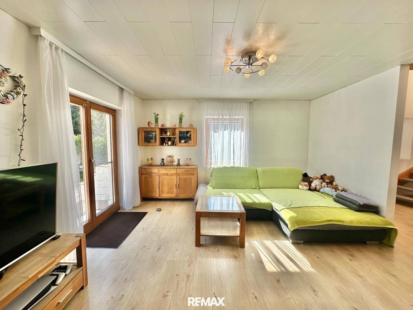Helles Wohnzimmer mit grünem Sofa, Fernseher und direktem Zugang zur Terrasse.