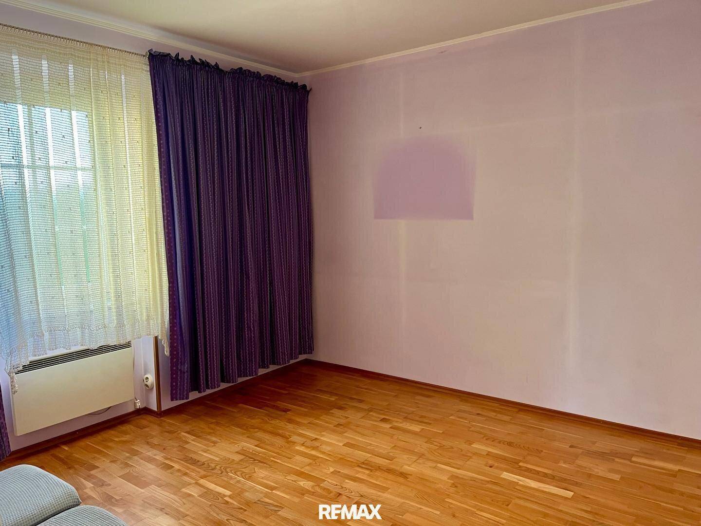 Helles Schlafzimmer mit Holzboden und lila Vorhängen, bereit zur individuellen Gestaltung.