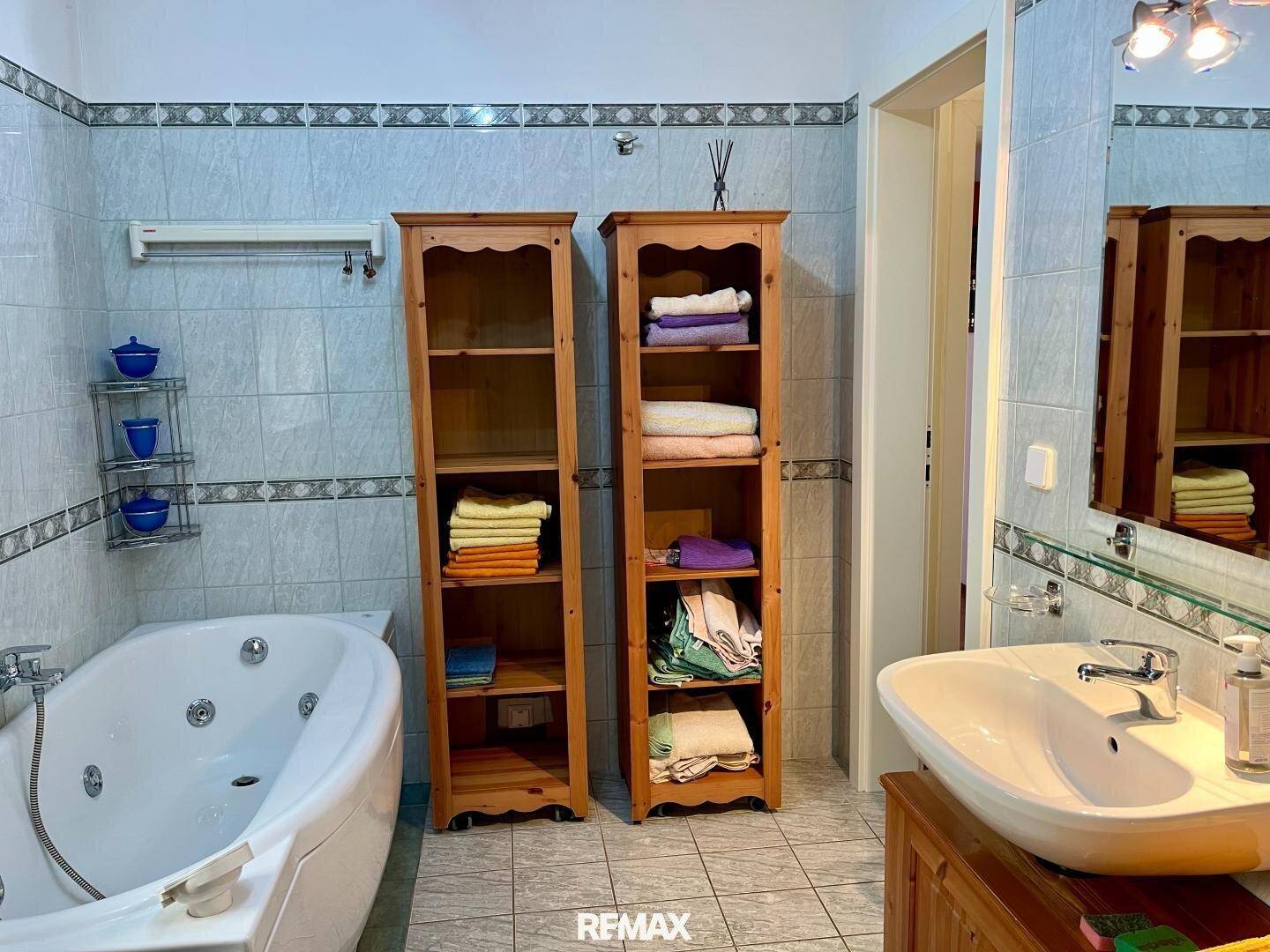 Gefliestes Badezimmer mit Whirlpool-Badewanne, Einzelwaschbecken und Holzregalen.