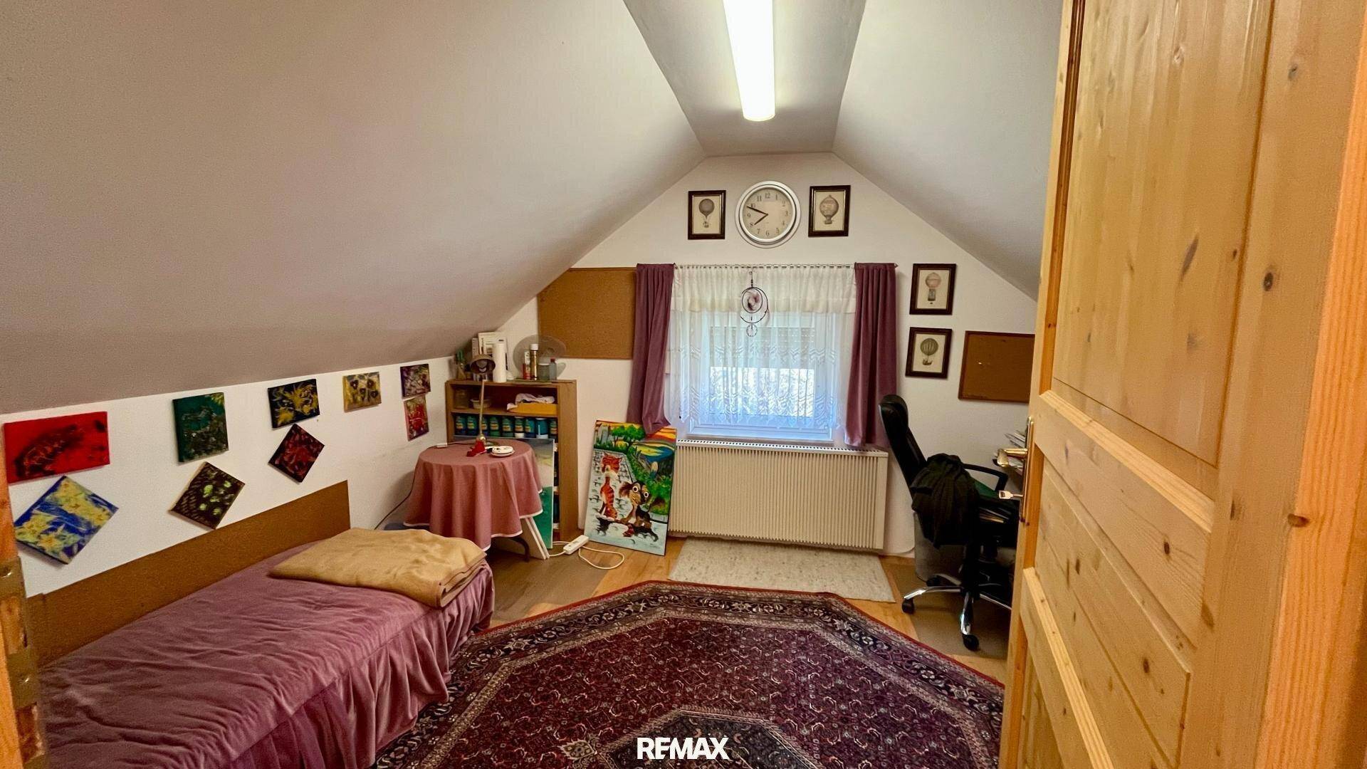Schlafzimmer im Dachgeschoss mit Einzelbett, Schreibtisch und schrägen Wänden.