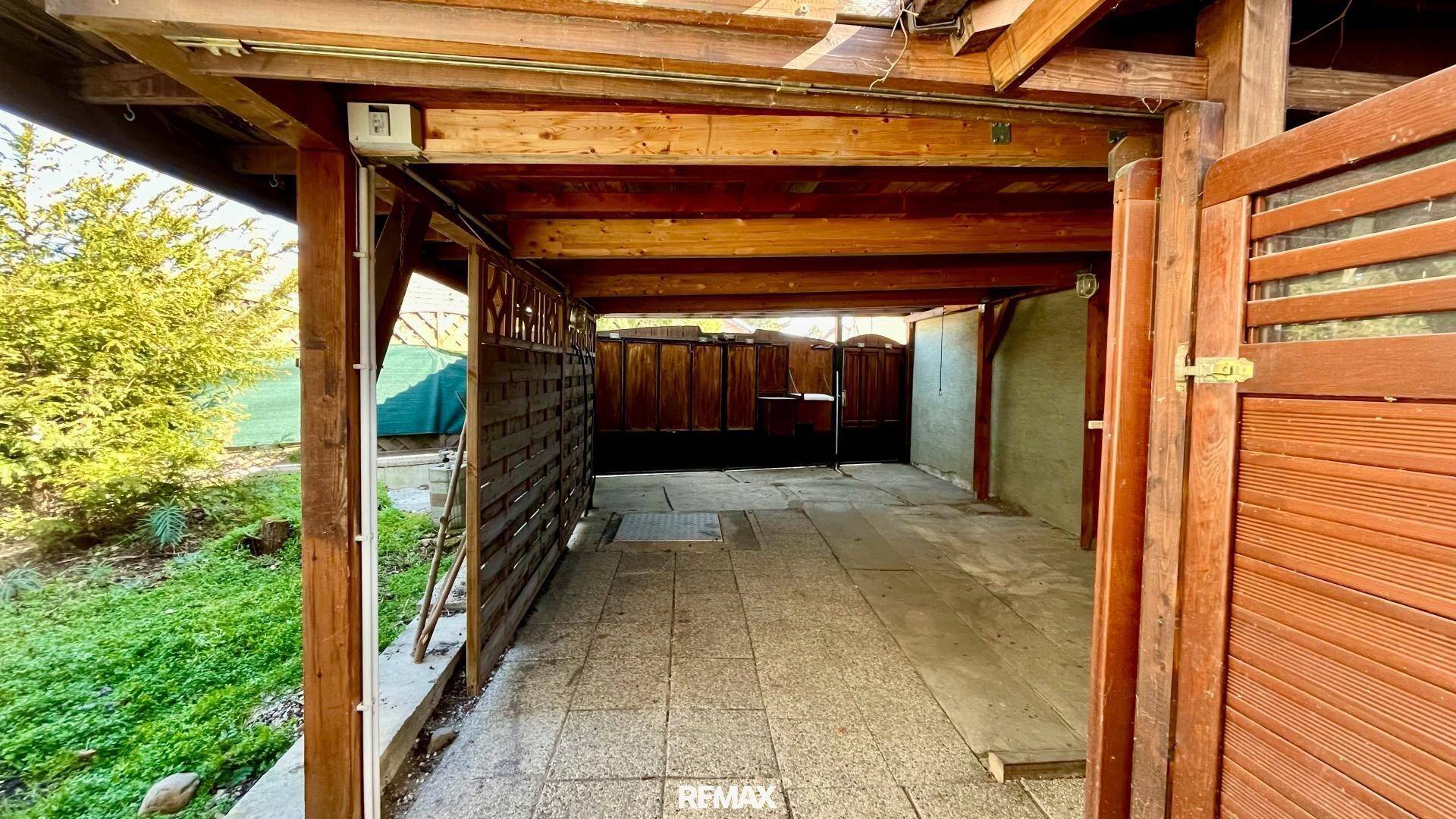 Geräumiger Holz-Carport mit gepflastertem Boden, bietet Schutz für Fahrzeuge.