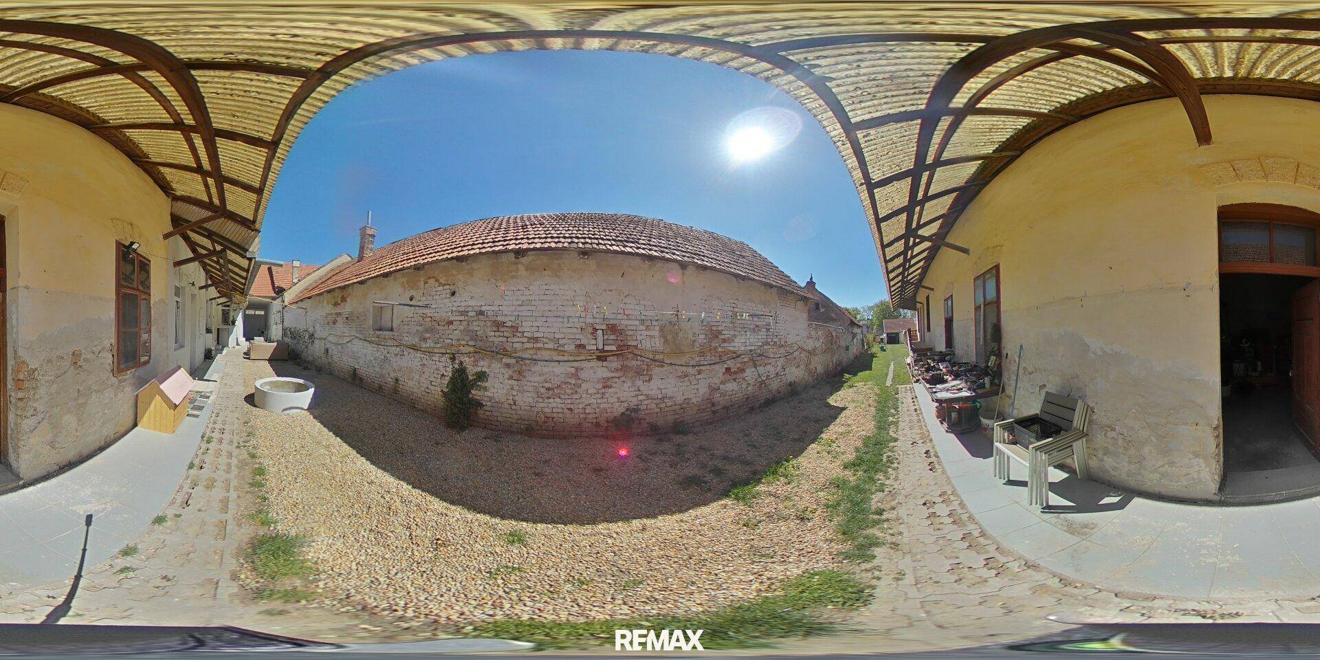 Sonniger Innenhof mit alter Ziegelmauer und überdachtem Gangbereich, ideal für Entspannung.