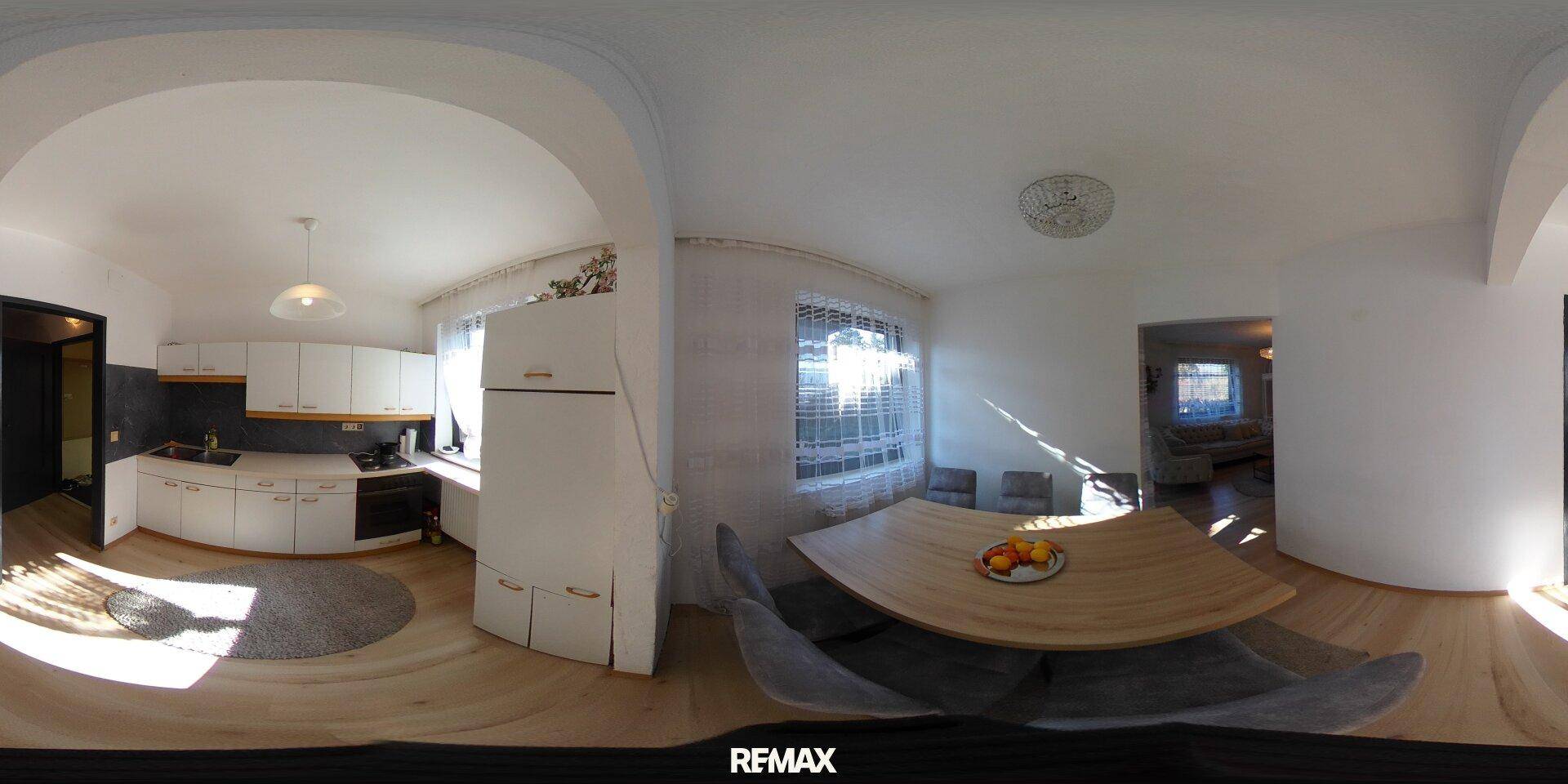 Panoramablick auf eine helle Wohnküche mit weißen Schränken und Esstisch.