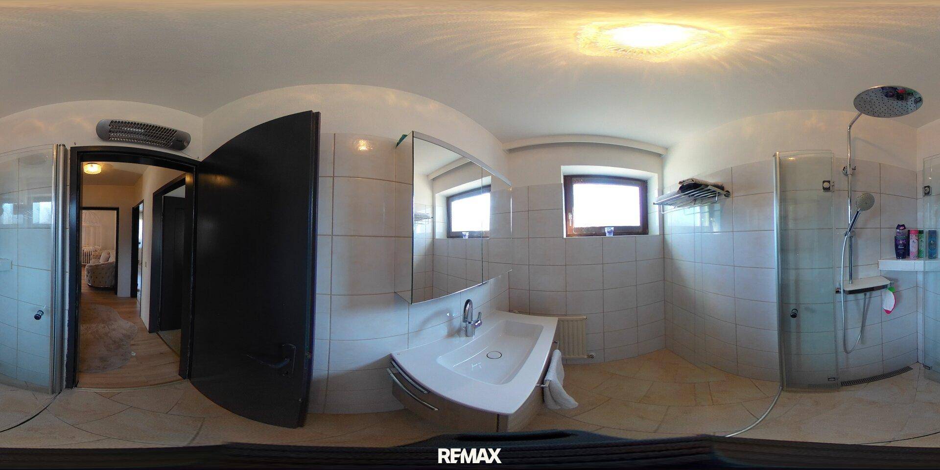 Panoramablick auf ein Badezimmer mit Dusche, Waschbecken und weißen Fliesen.