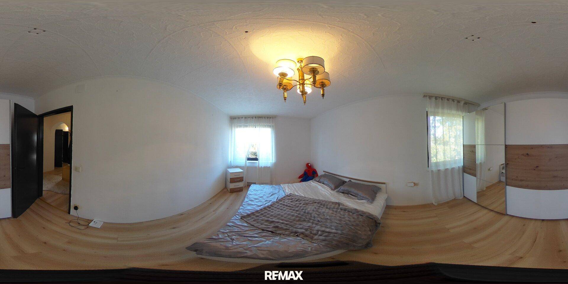 Panoramablick auf ein Schlafzimmer mit Bett, Holzboden und Fenster.
