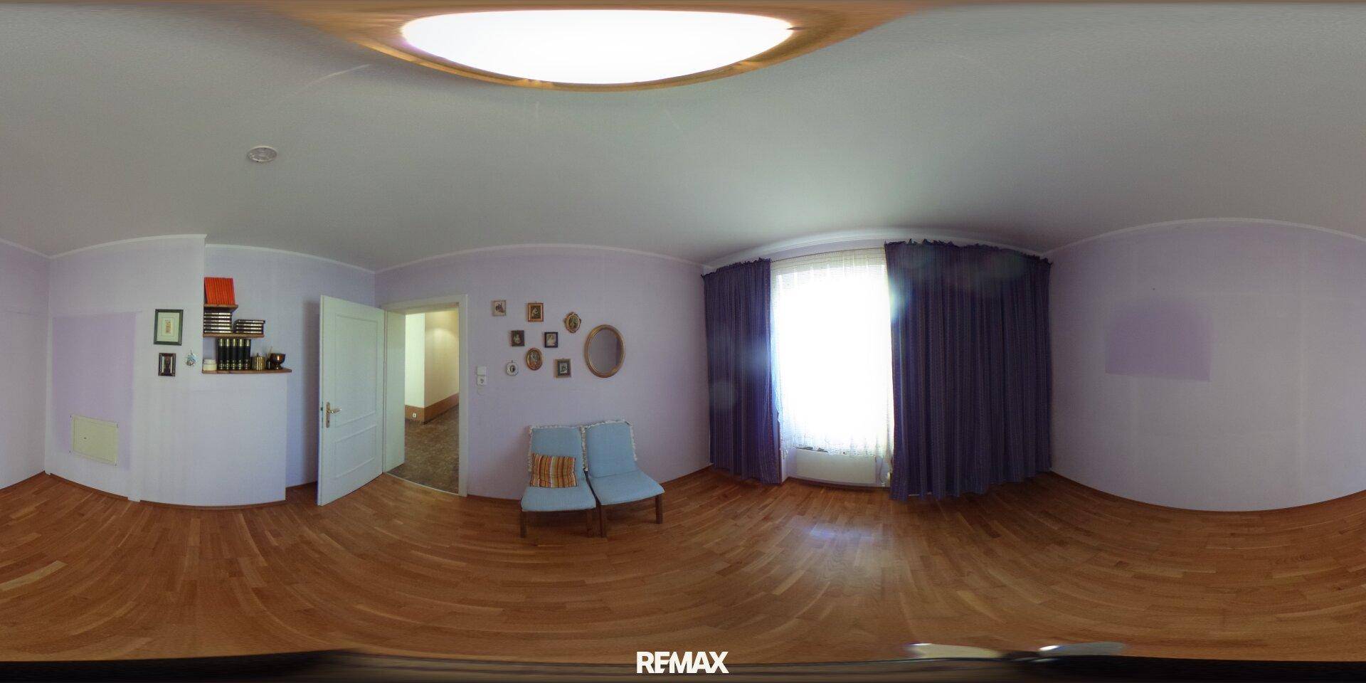 Helles Wohnzimmer mit Holzboden, zwei Sesseln und dunklen Vorhängen, die für eine gemütliche Atmosphäre sorgen.