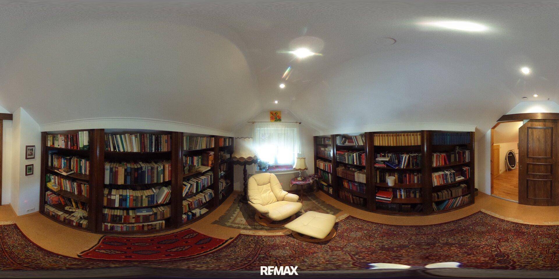 Gemütliche Bibliothek mit raumhohen Bücherregalen, einem bequemen Sessel und Teppichboden.