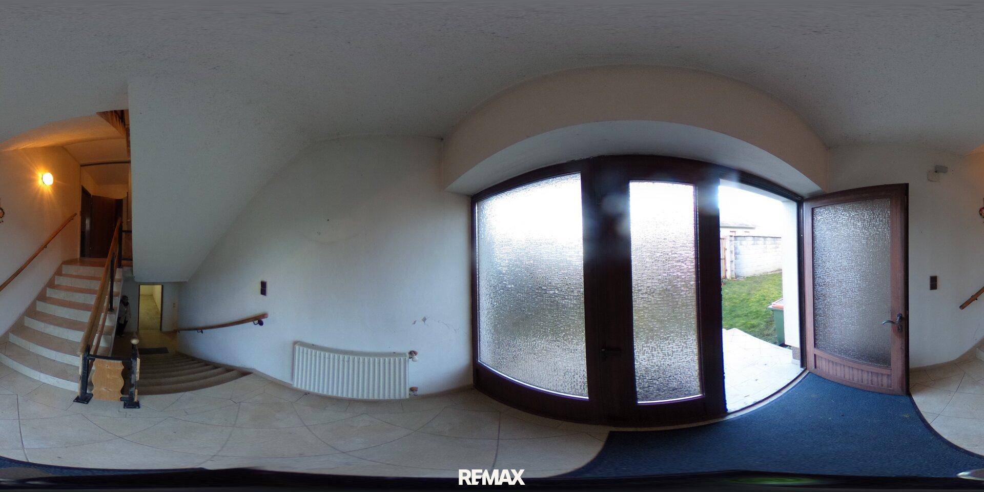 Eingangsbereich mit großer Glastür und Fliesenboden, führt zur Holztreppe und weiteren Räumen.
