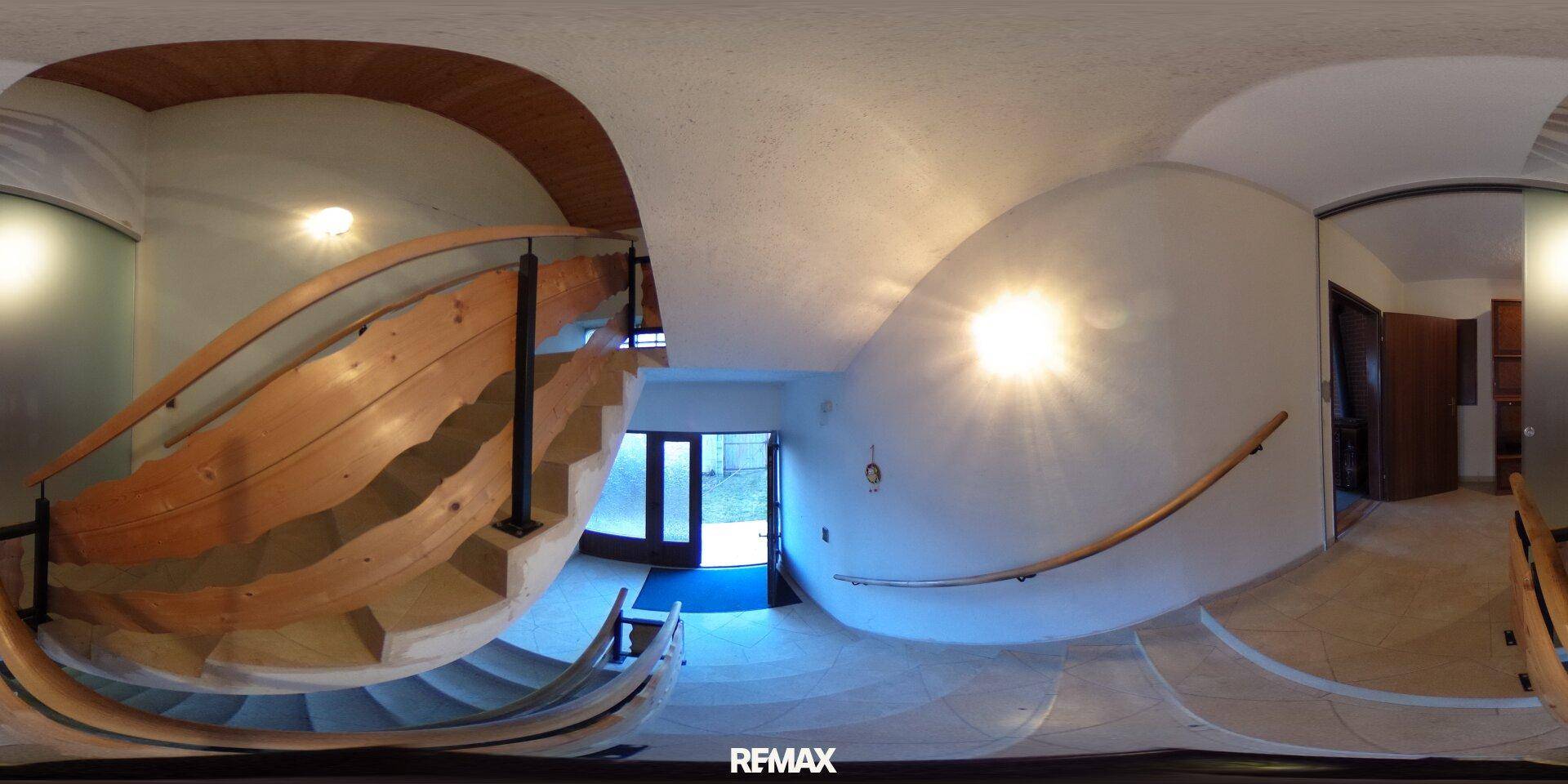 Heller Eingangsbereich mit geschwungener Holztreppe und Fliesenboden, führt zu weiteren Räumen.