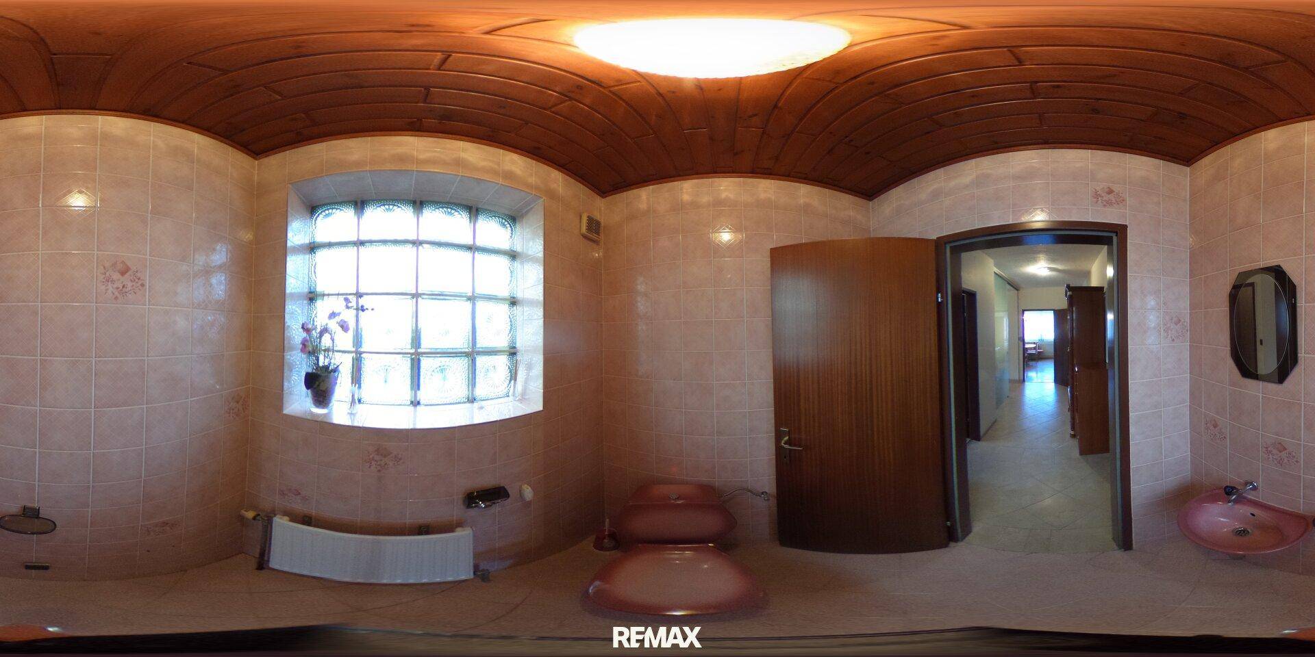 Badezimmer mit WC, Waschbecken und Fenster, ausgestattet mit hellen Fliesen und Holzdecke.