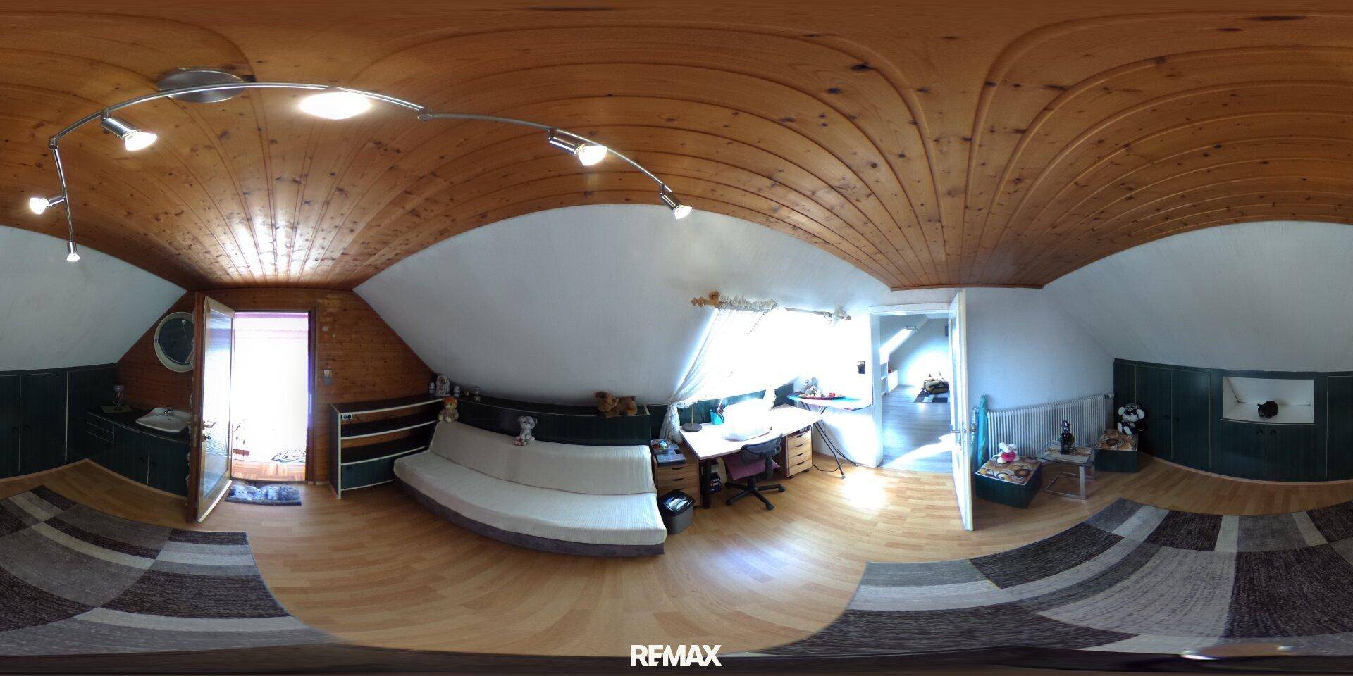 Gemütliches Dachzimmer mit Holzdecken, Bett, Schreibtisch und Sofa, ideal als Schlaf- oder Arbeitsbereich.