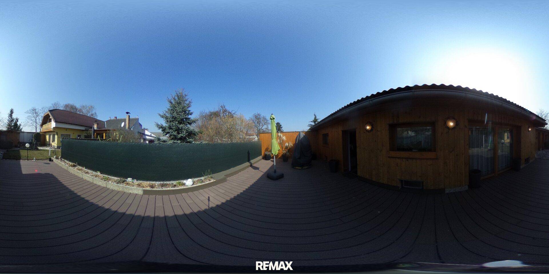Große Holzterrasse mit Hecke und Zugang zu einem Holzhaus, ideal für Entspannung im Freien.