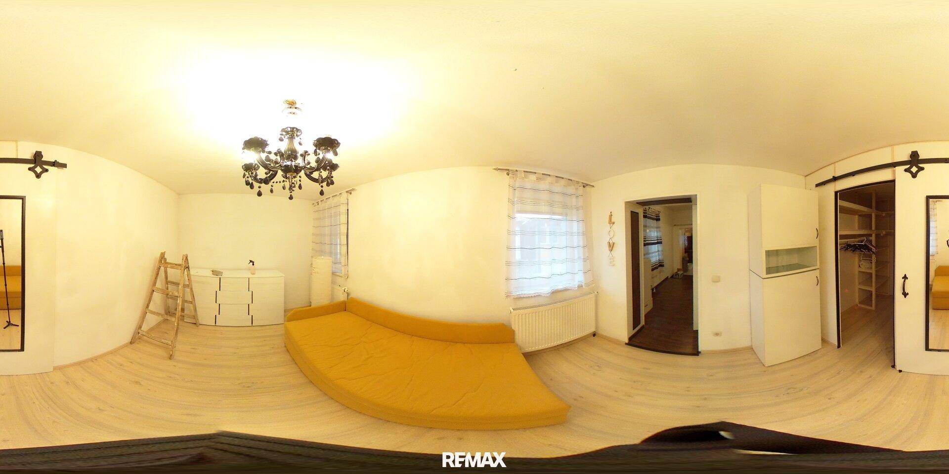 Panoramaaufnahme eines Schlafzimmers mit hellem Laminatboden und gelbem Schlafsofa.