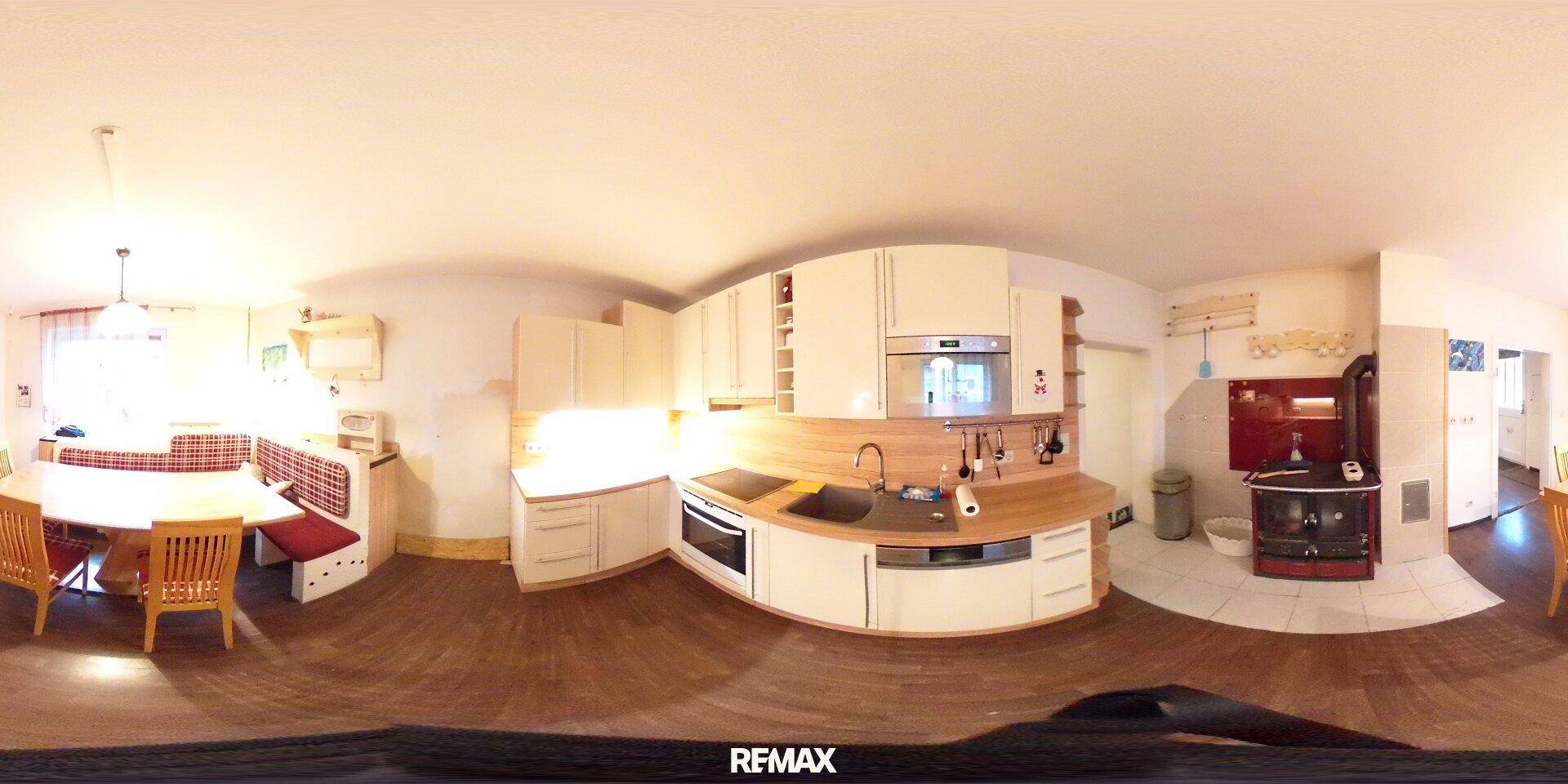 Panoramaaufnahme einer geräumigen Wohnküche mit Einbauküche, Essbereich und Holzofen.