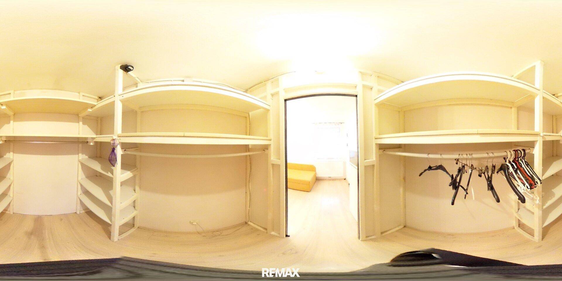 Panoramaaufnahme eines begehbaren Kleiderschranks mit offenen Regalen und Kleiderstangen.