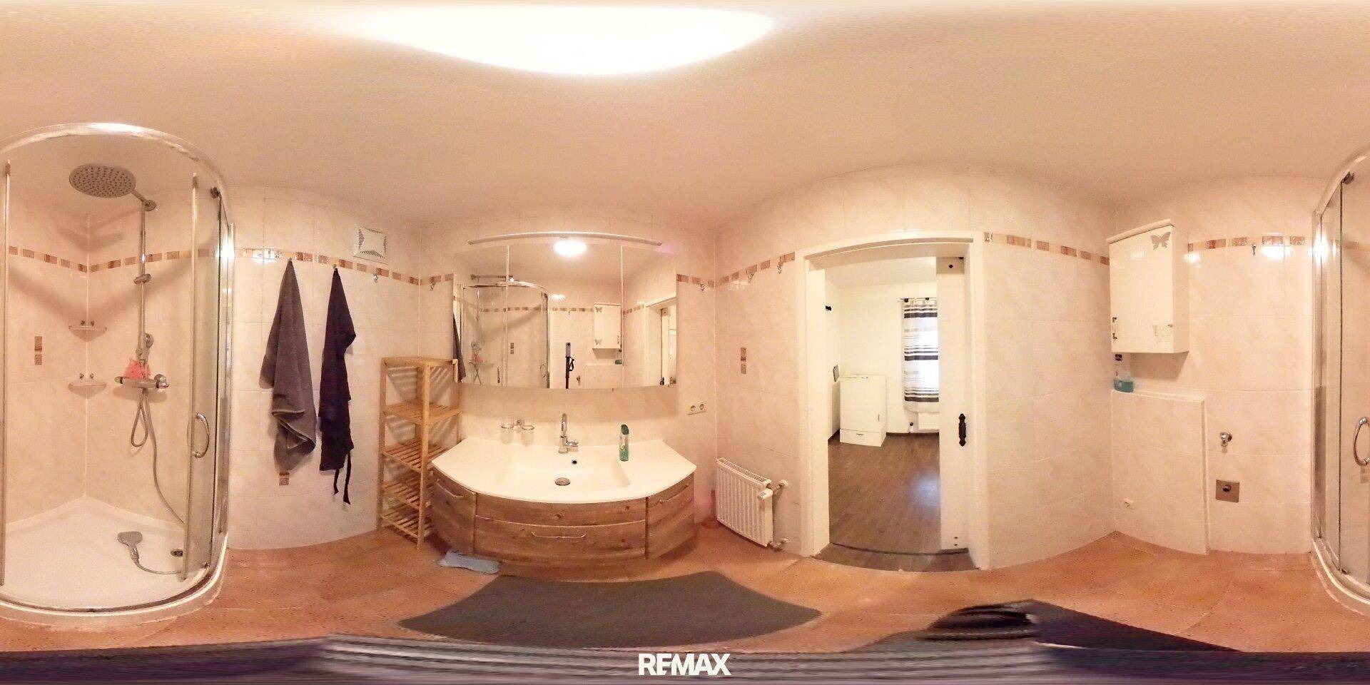 Panoramaaufnahme eines Badezimmers mit Duschkabine, Waschbecken und großen Fliesen.