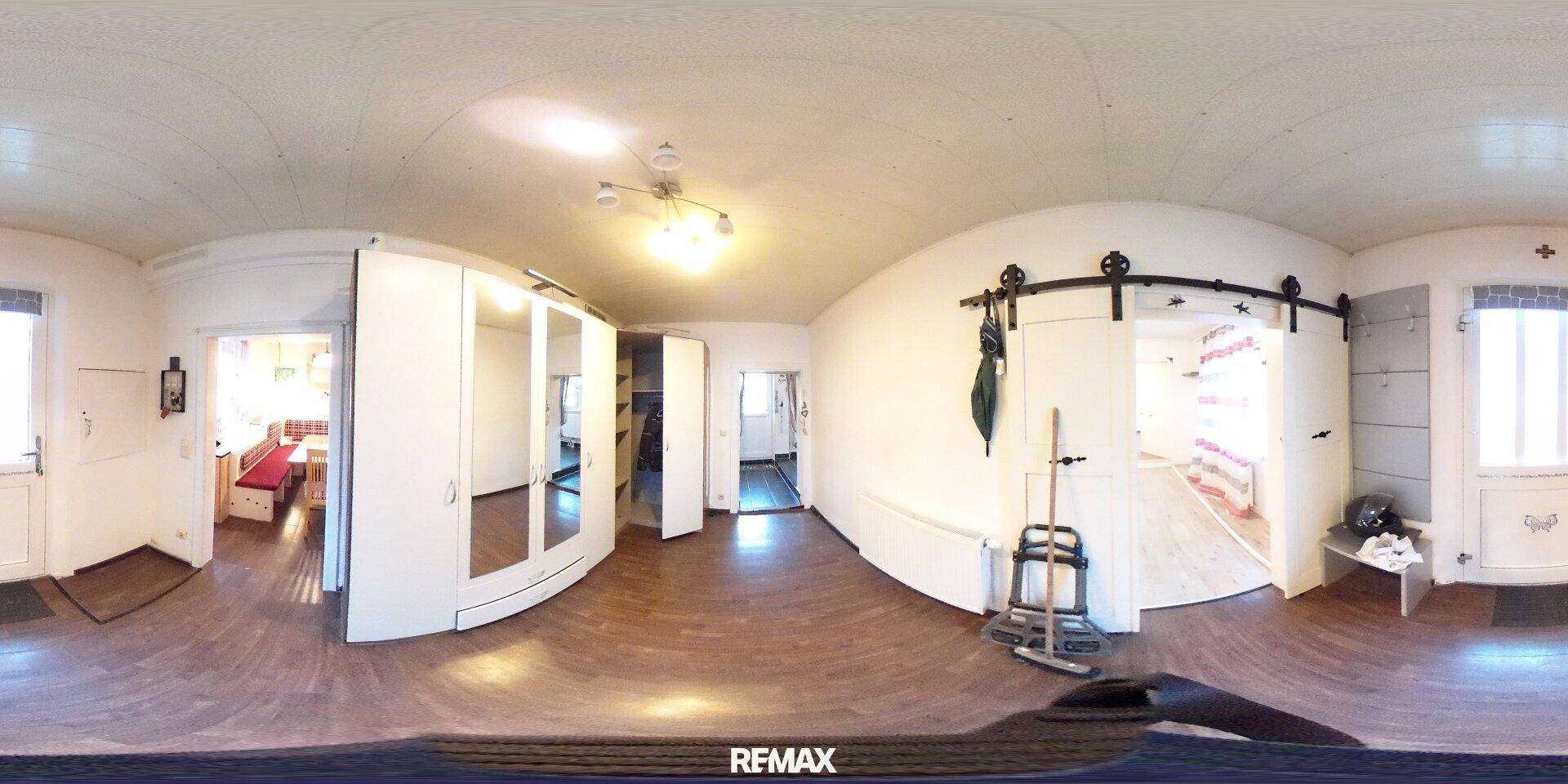 Panoramaaufnahme eines Flurs mit weißen Schränken, Holzfußboden und Schiebetüren.