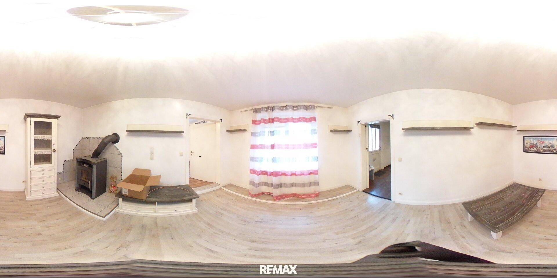 Panoramaaufnahme eines Wohnzimmers mit hellem Laminatboden und Holzofen.