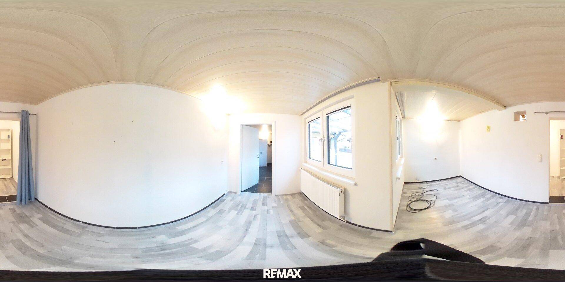 Panoramaaufnahme eines leeren Raumes mit hellem Holzboden und einem Fenster.