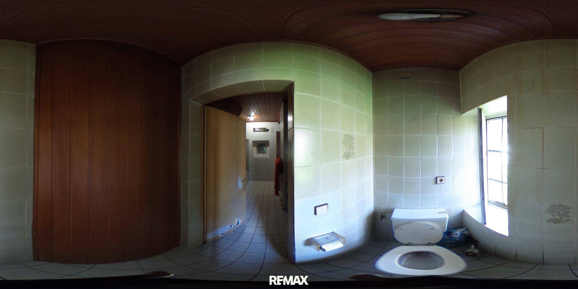 Einfache Toilette mit Fliesen an den Wänden und einem kleinen Fenster, das Renovierung benötigt.