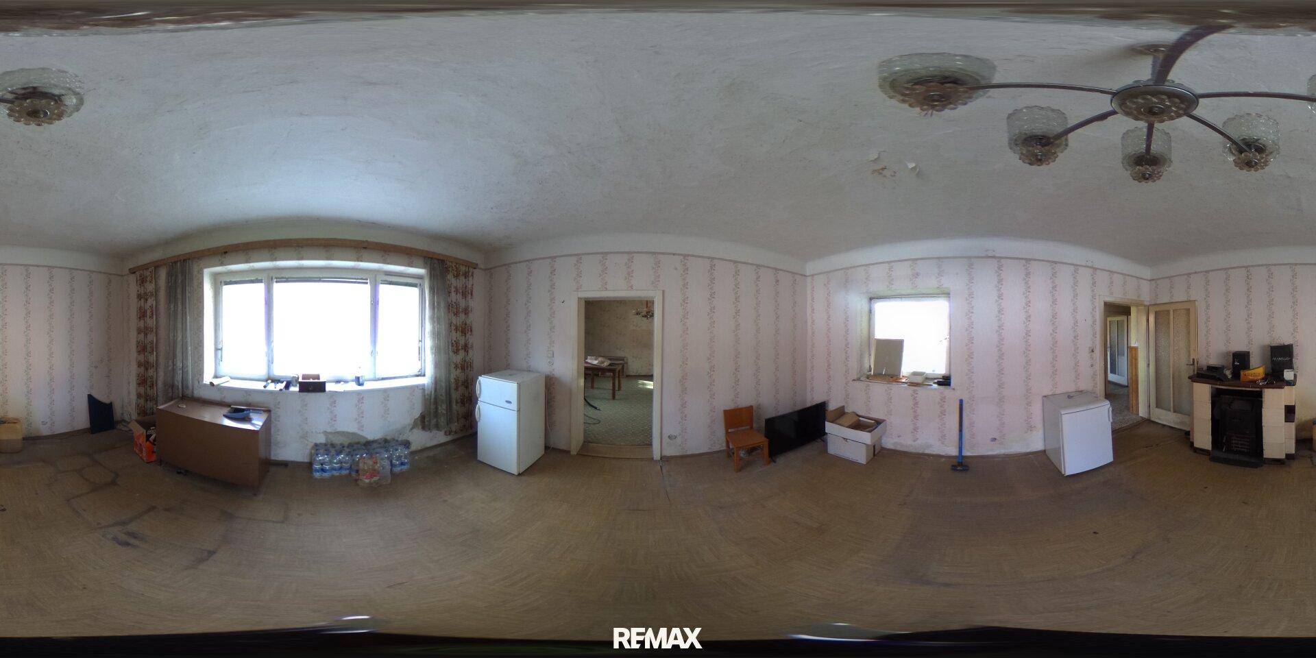Geräumiges Wohnzimmer mit Tapeten, Holzboden und großen Fenstern, das renovierungsbedürftig ist.