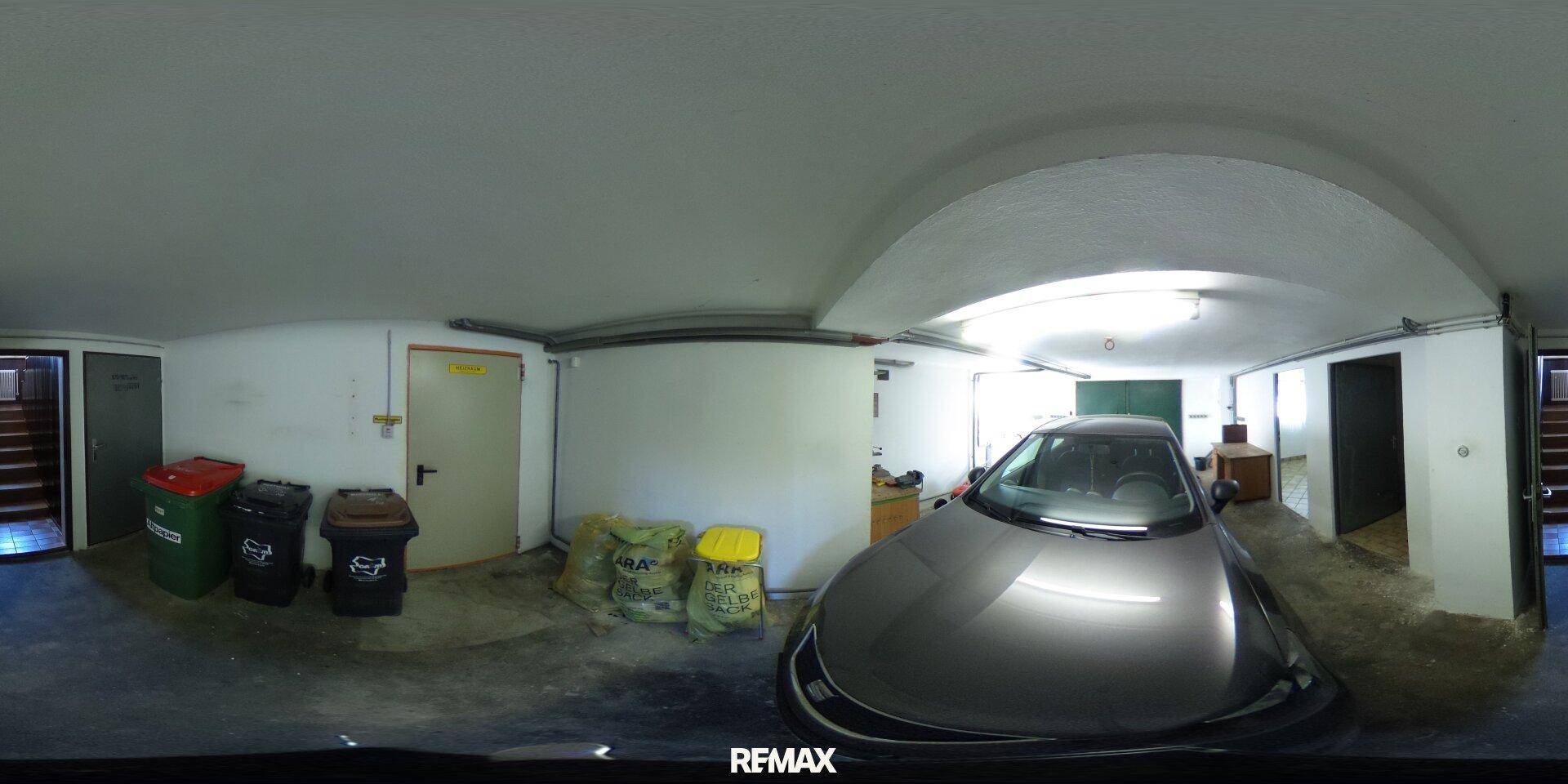 Geräumige Garage mit einem Auto, Abfallbehältern und Stauraum.