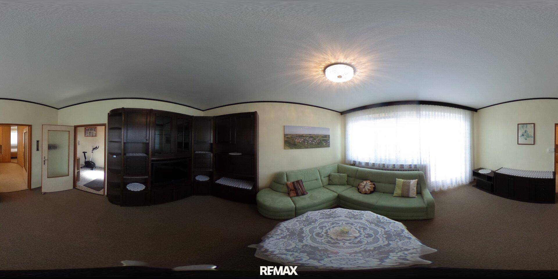 Gemütliches Wohnzimmer mit großem grünem Sofa, Couchtisch und einem breiten Fenster.
