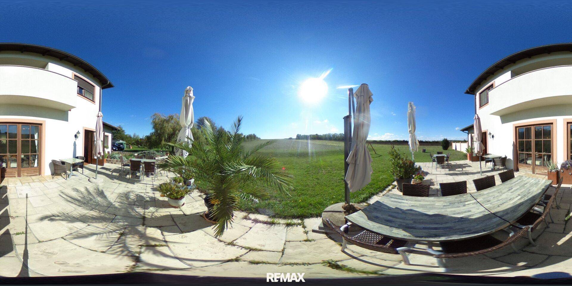 Große Außenterrasse mit Sitzgelegenheiten, Sonnenschirmen und weitem Blick auf die grüne Landschaft.