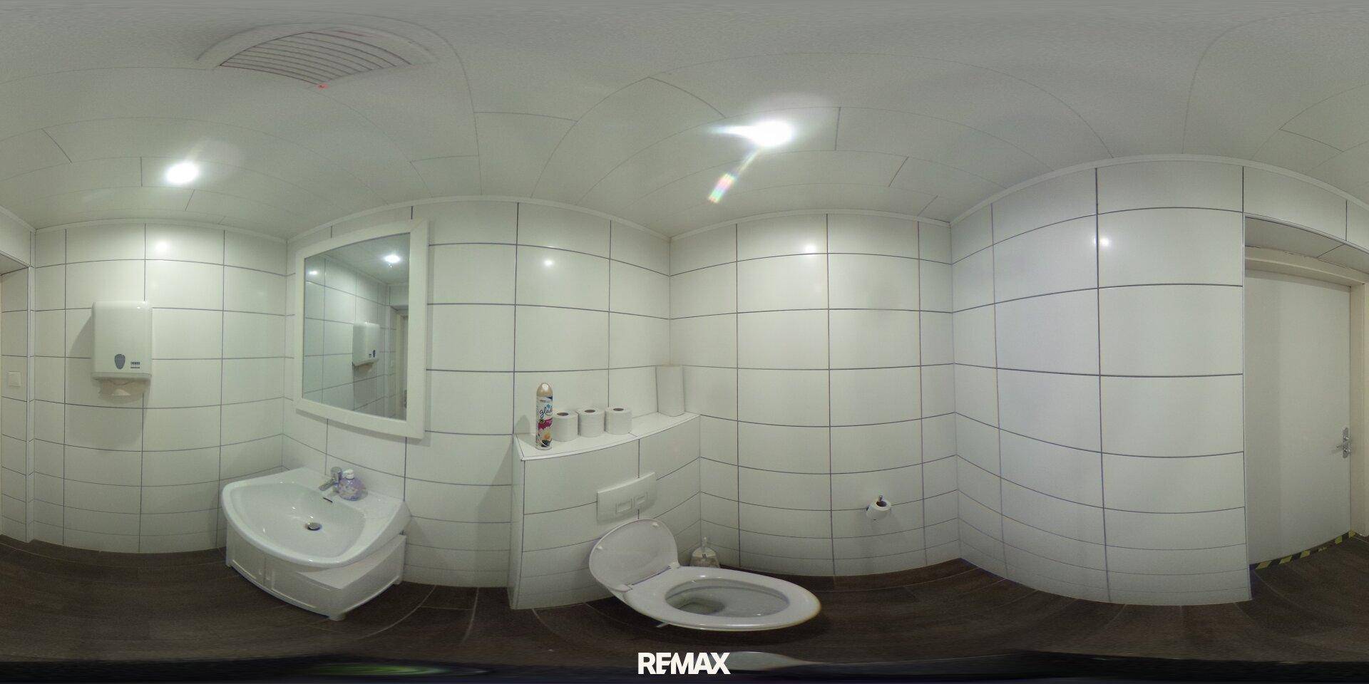 Helles Badezimmer mit weißen Fliesen, Waschbecken, Toilette und Spiegel, in gutem Zustand.