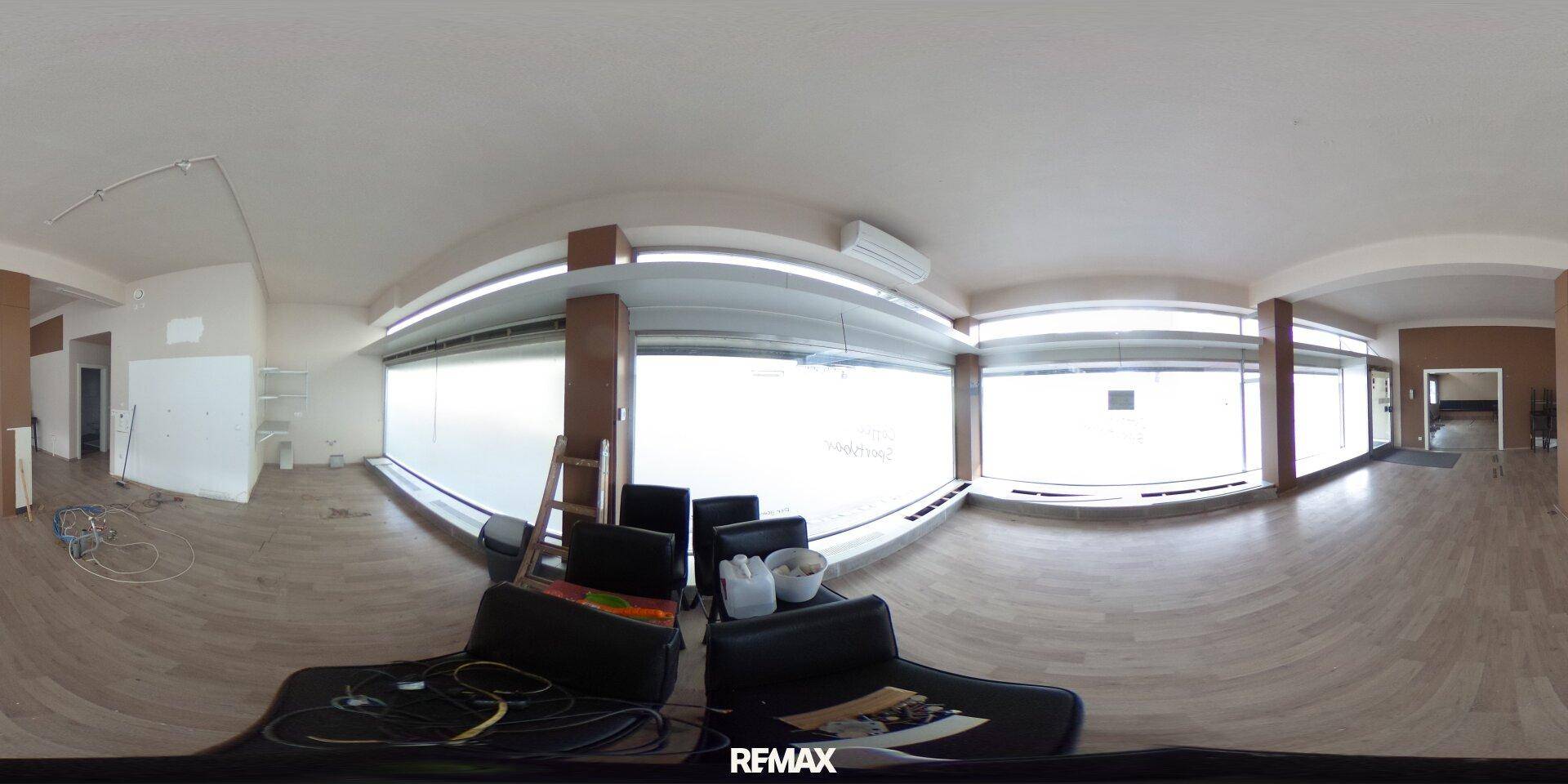 Panoramaansicht eines Gewerberaums mit Holzboden, großen Fenstern und sichtbaren Installationsarbeiten.