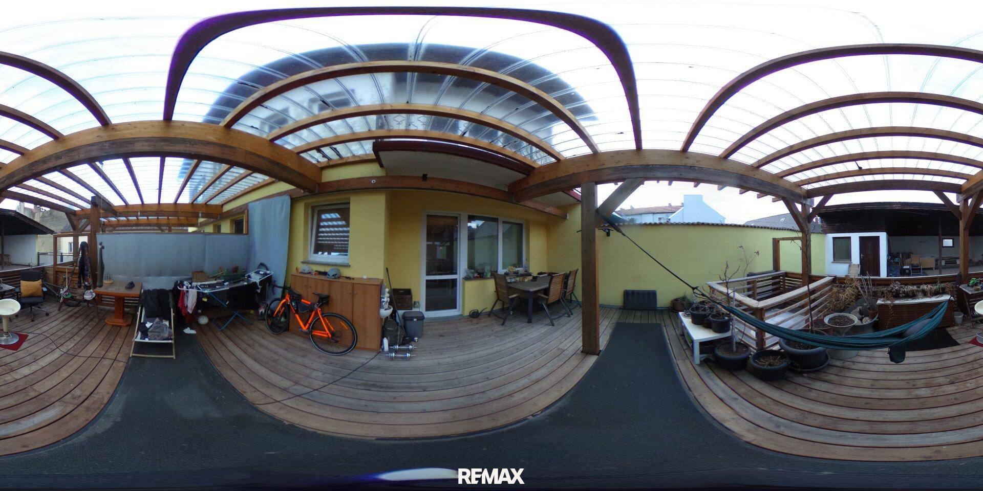 Überdachte Holzterrasse mit Sitzgelegenheiten und Fahrrad, bietet einen geschützten Außenbereich.
