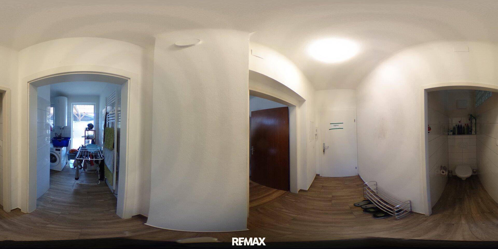 Heller Flur mit Holzboden, der zu verschiedenen Räumen führt, inklusive Badezimmer und Waschküche.