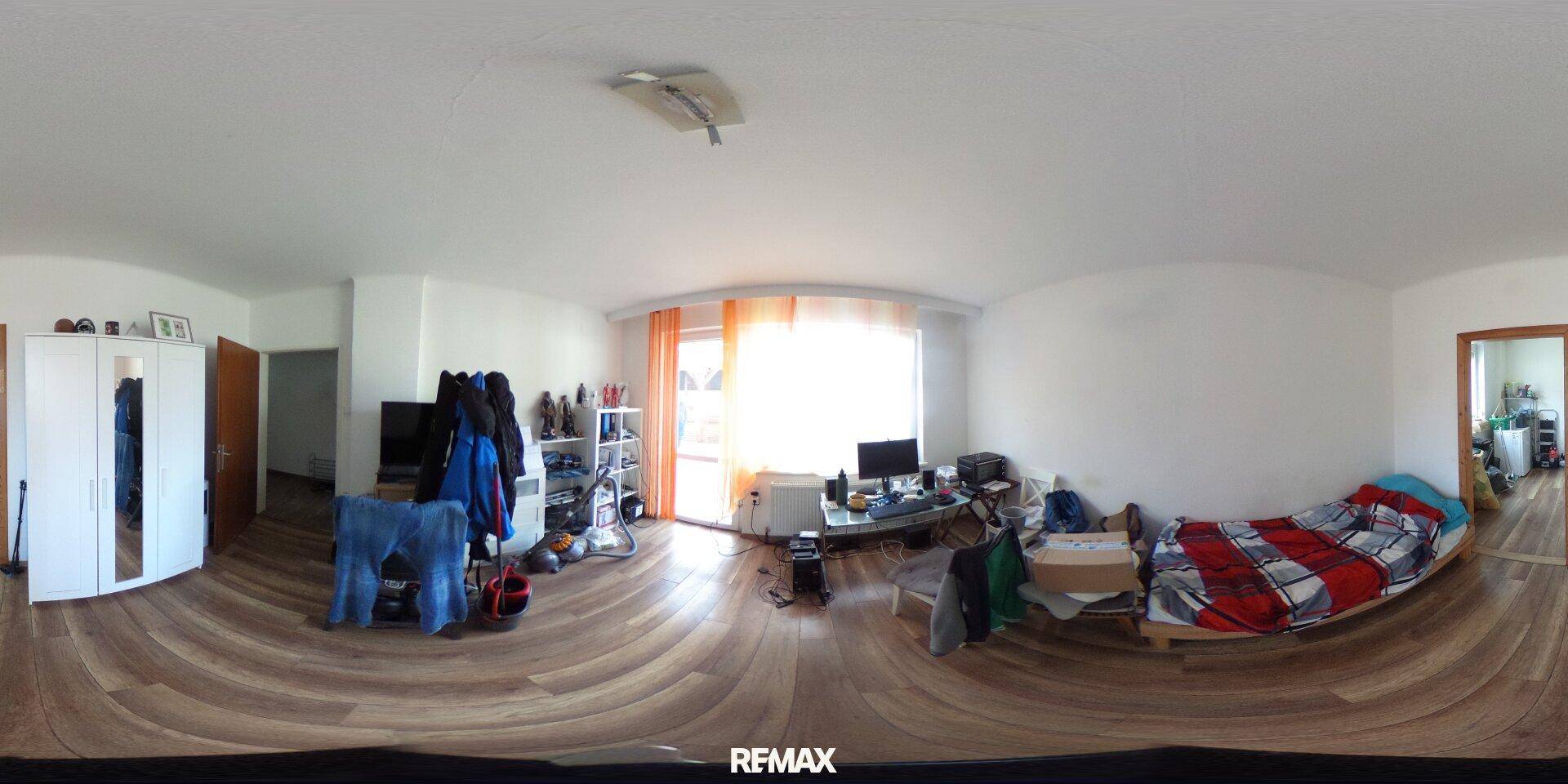Geräumiges Schlafzimmer mit Bett, Schrank und Schreibtisch, viel natürliches Licht durch großes Fenster.
