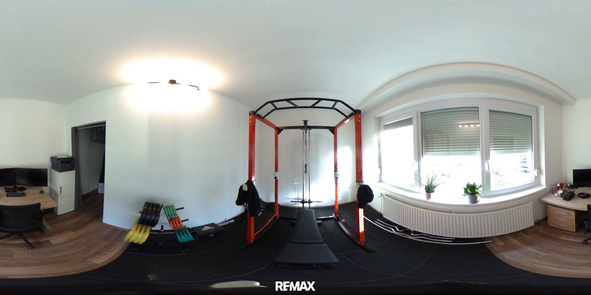Fitnessraum mit Trainingsgeräten, großem Fenster und Holzboden, ideal für Sport zu Hause.