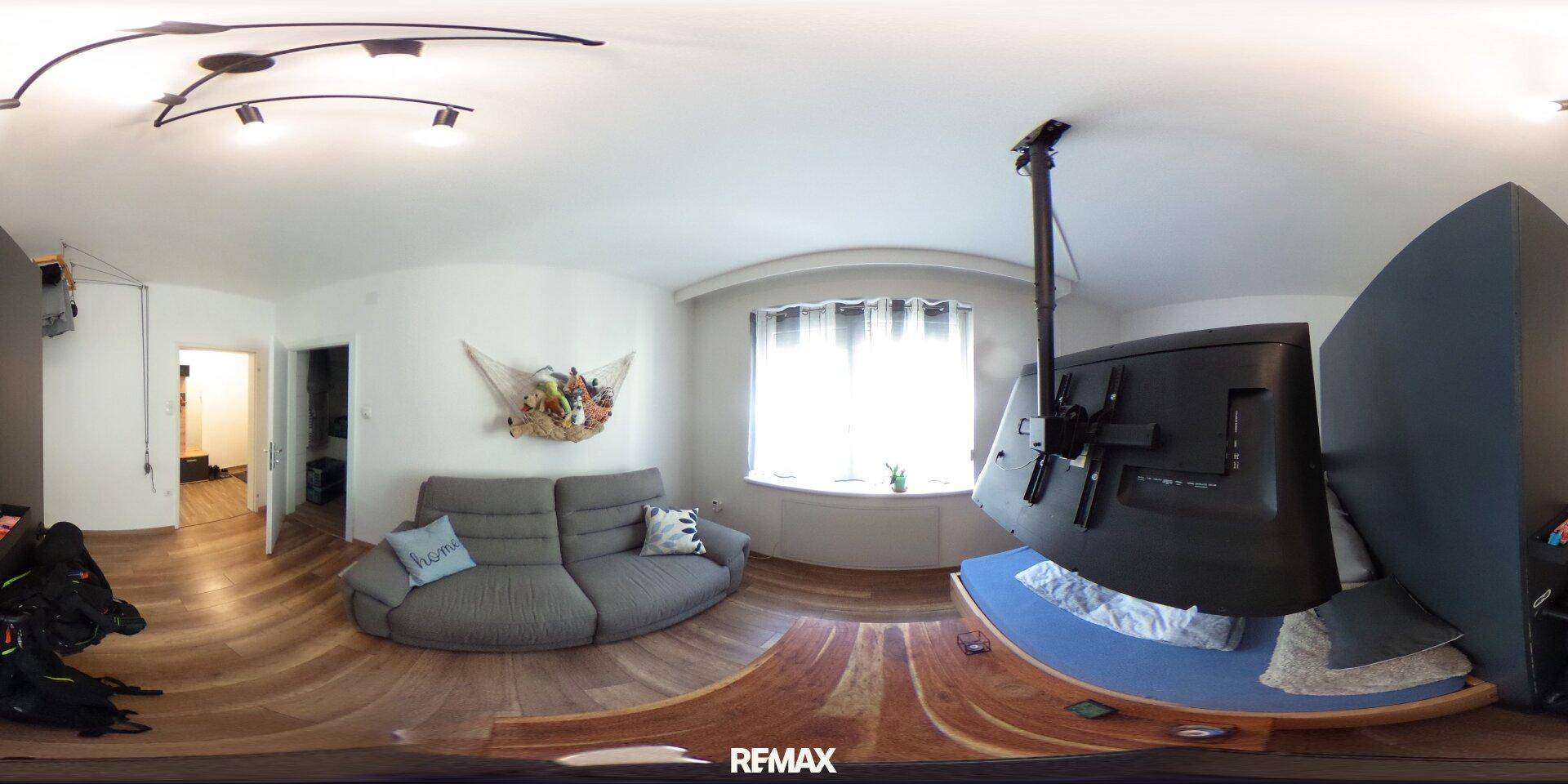 Gemütliches Wohnzimmer mit Sofa, Holzboden und großem Fenster, ideal zum Entspannen.