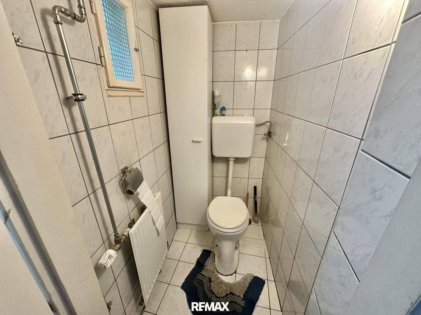 Kleines gefliestes WC mit Toilette, Waschbecken und Fenster.