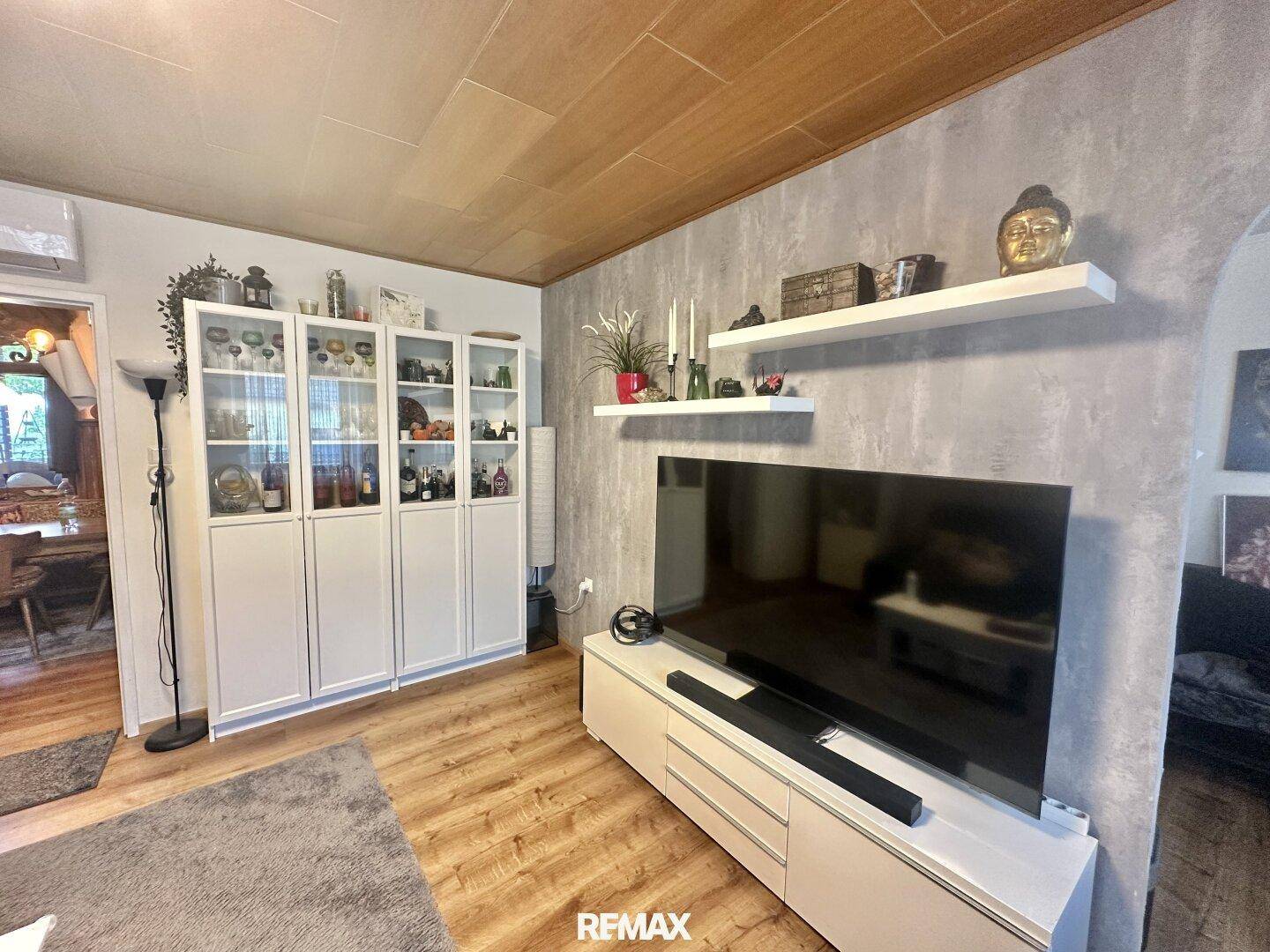 Heller Wohnbereich mit Fernseher, weißen Regalschränken und Holzboden.
