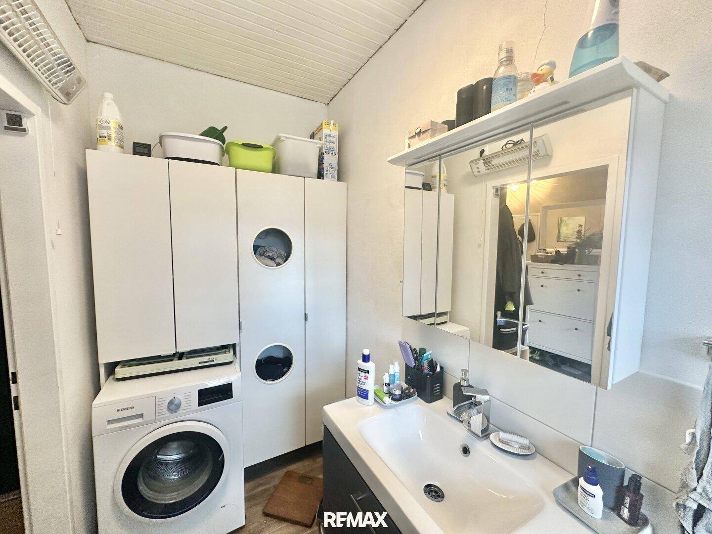 Badezimmer mit Waschbecken, Spiegelschrank und integrierter Waschmaschine.