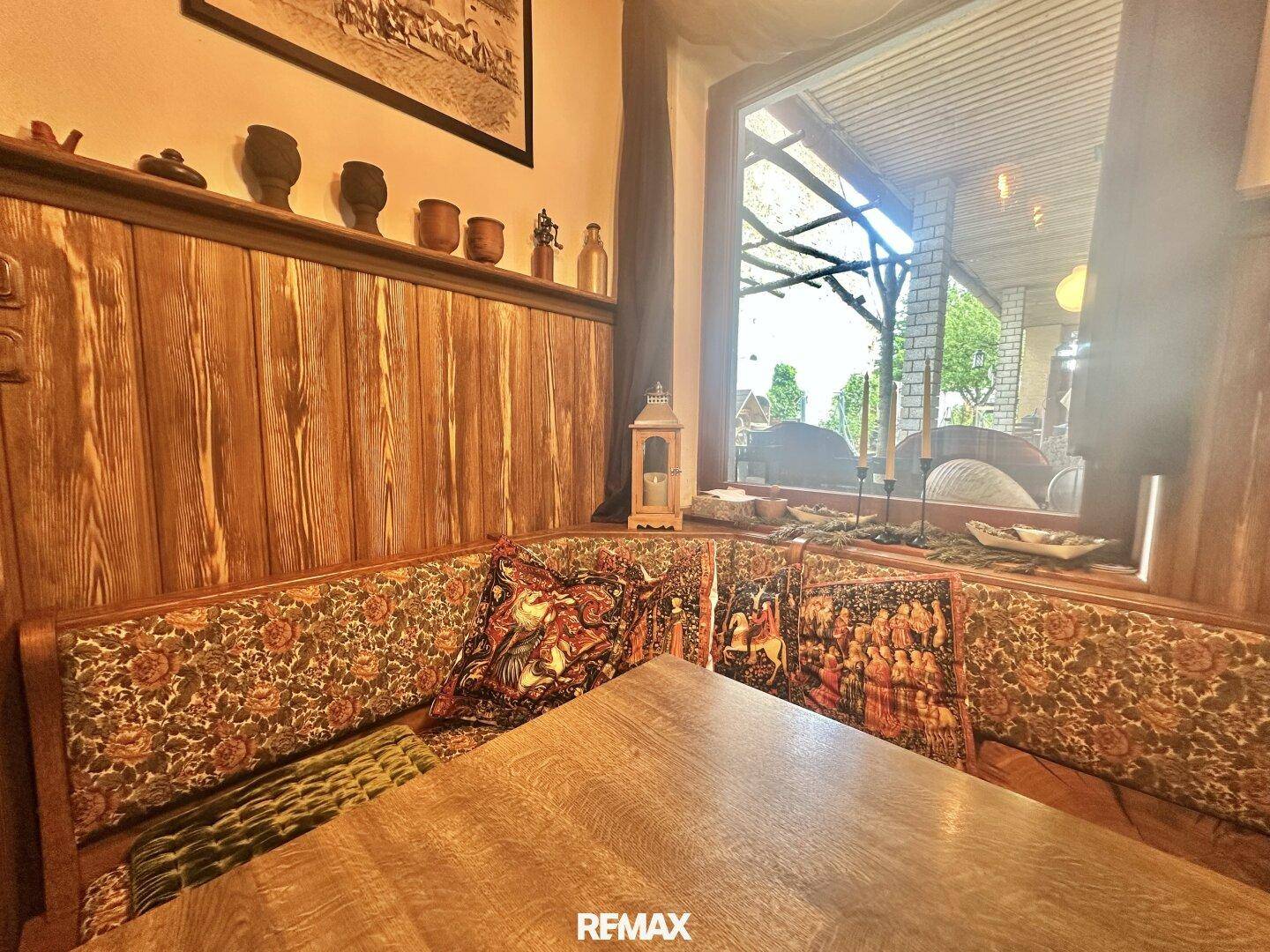 Traditionelle Sitzecke mit Holztisch und gepolsterten Bänken neben einem großen Fenster.
