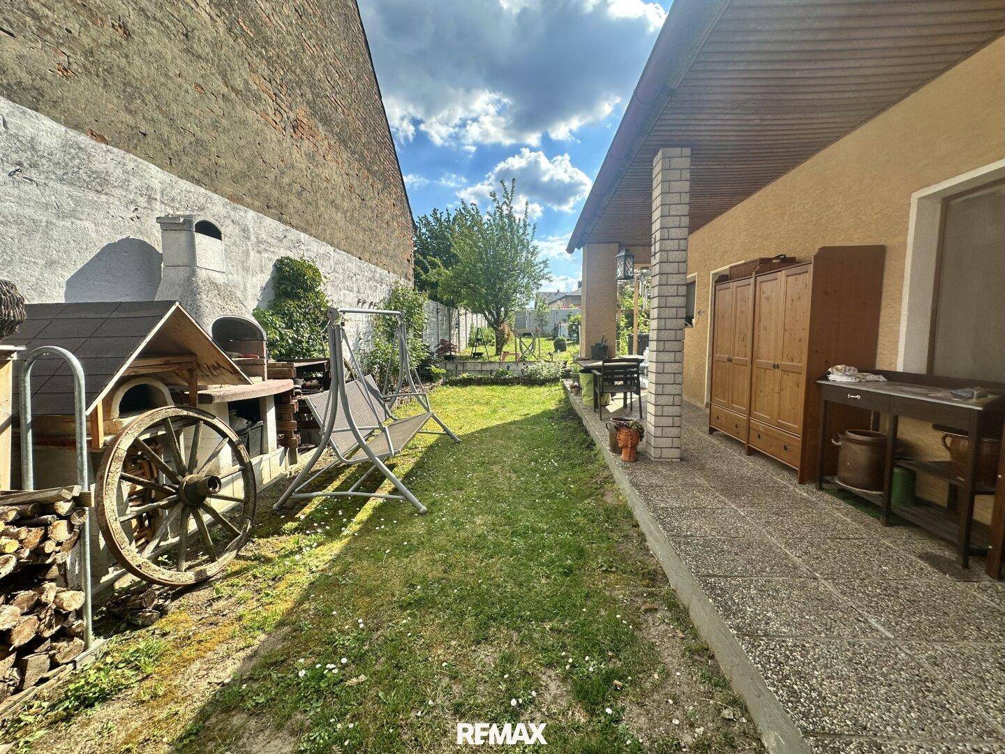 Blick vom überdachten Patio in den Garten mit Rasenfläche und Grillbereich.