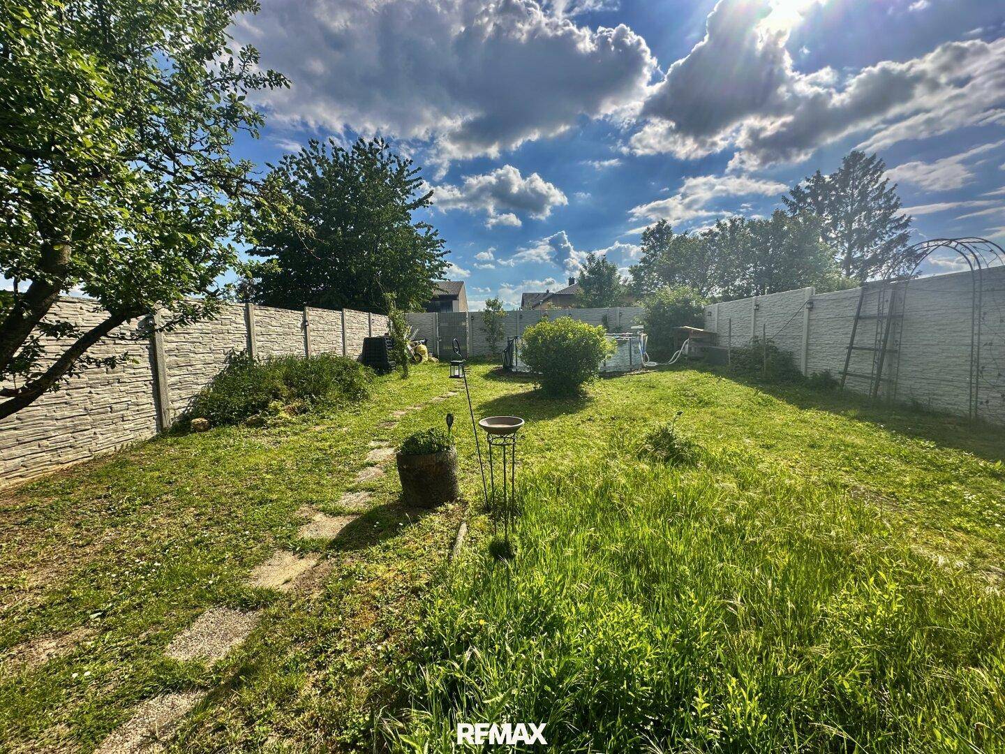 Weitläufiger Garten mit Rasenfläche, Zaun und einem Pool in der Ferne.