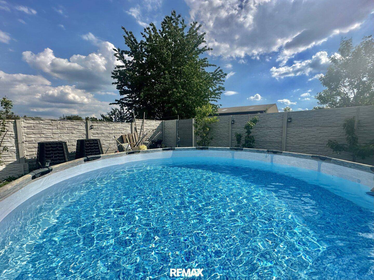 Aufstellpool im Garten an einem sonnigen Tag, umgeben von einem Zaun und grünen Bäumen.