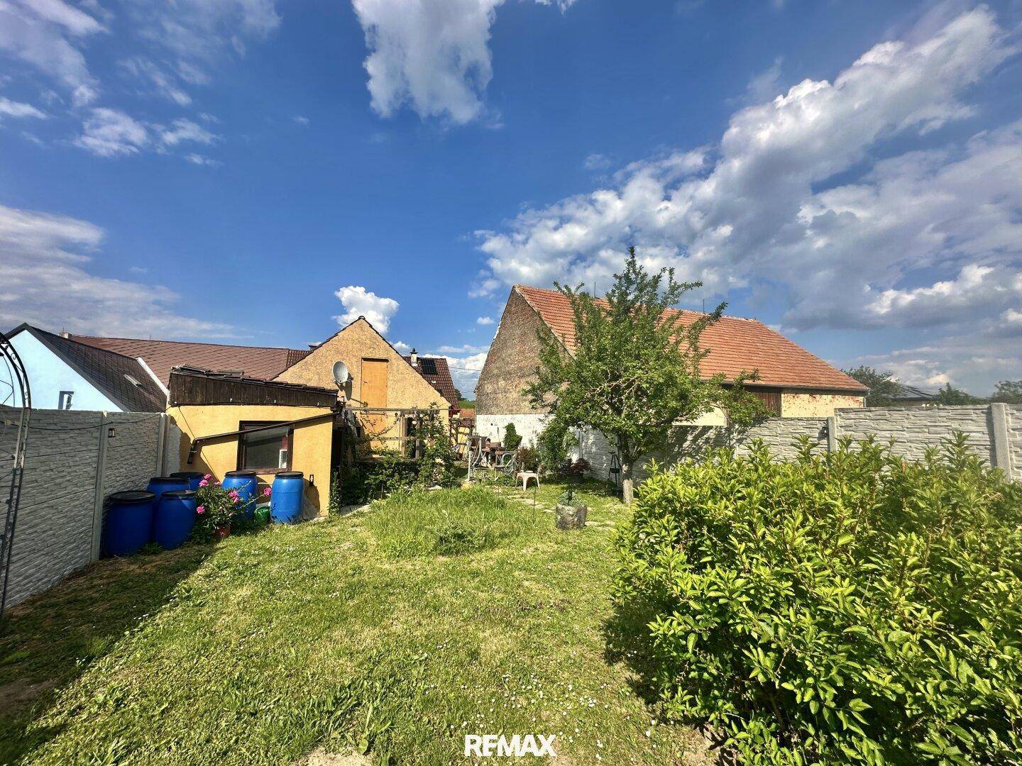 Großer Gartenbereich mit Rasenfläche und älteren Gebäuden im Hintergrund unter blauem Himmel.