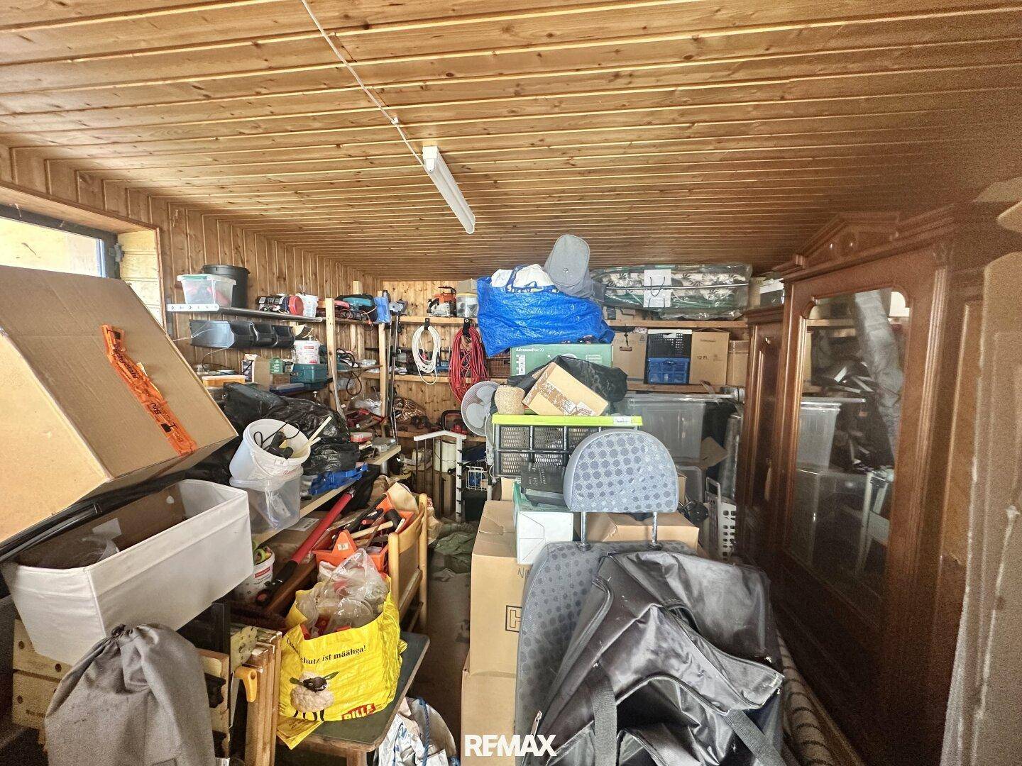 Vollgestopfter Abstellraum mit Holzverkleidung an der Decke und zahlreichen Kartons und Gegenständen.