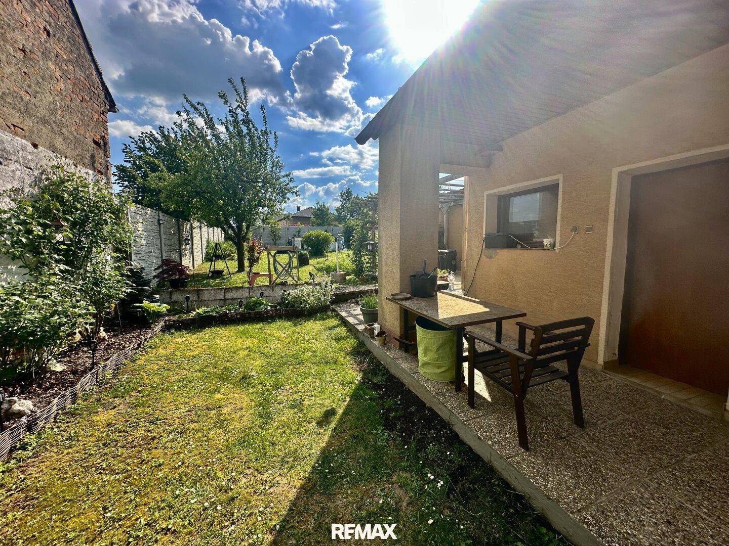 Sonniger Gartenbereich mit kleiner Terrasse und Gartenmöbeln neben dem Gebäude.